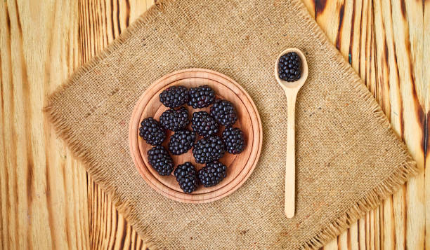 istock Fresh ripe blackberries in wooden plate and spoon on rustic table, top view 1168569203