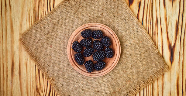 istock Fresh ripe blackberries in wooden plate on rustic table, top view 1168569233