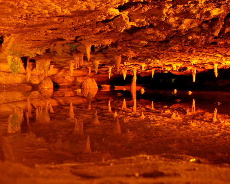 An underground pool reflects stalactites above it bathed in a surreal light.