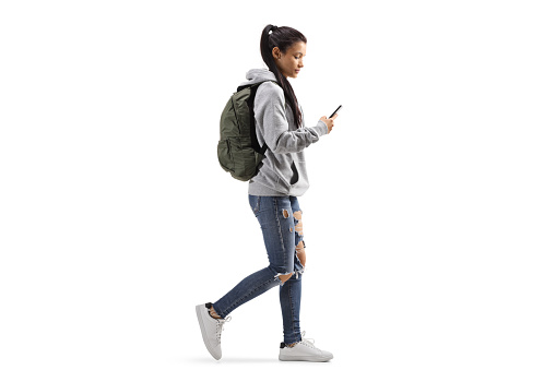 Female student with a backpack walking and looking into a mobile phone