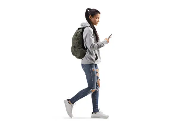 Photo of Female student with a backpack walking and looking into a mobile phone