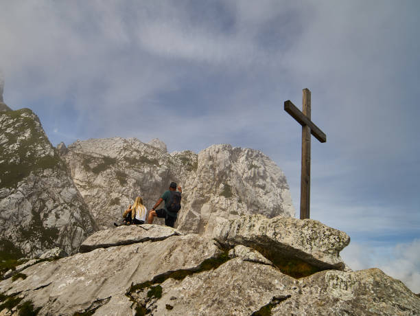 una donna bionda e un uomo con uno zaino ammirano le montagne della terra di werdenfelser accanto a una semplice croce puritana in legno. - puritanical foto e immagini stock