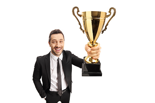 Happy young man in a suit holding a gold trophy cup isolated on white background