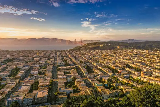 An aerial view from Golden Gate Park looking across the Avenues to the Presidio and Golden Gate Bridge just as the sun begins to set. Golden shadows across the row houses of San Francisco