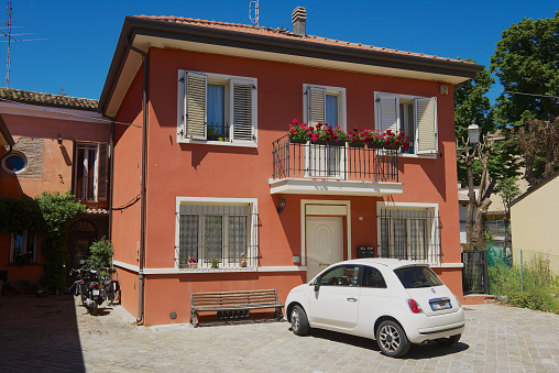 Rimini, Italy - May 13, 2013: White car parked at the red painted two floors residential building in Rimini, Italy.