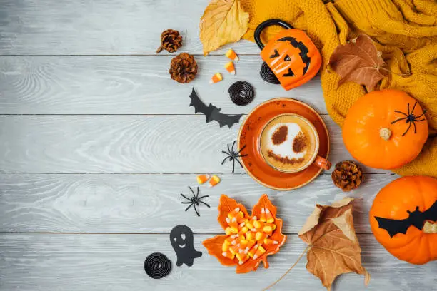 Photo of Halloween holiday background with coffee cup, pumpkin and autumn leaves on wooden table. Top view from above. Flat lay