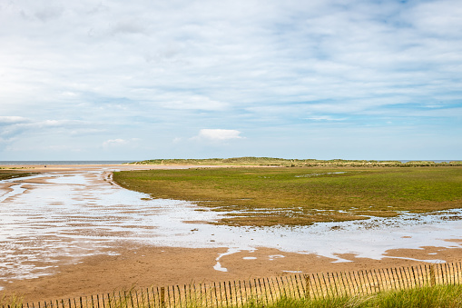 Wide-angle view of the beach and dunes at the Holkham National Nature Reserve in the United Kingdom on a cloudy Summer day, one of the most unspoilt and beautiful stretches of sand in the country.