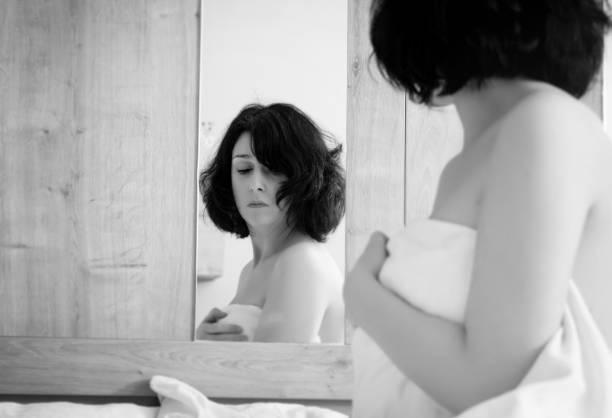 istock Thoughtful Woman Covering Body With Sheet While Reflection On Mirror 1168590958