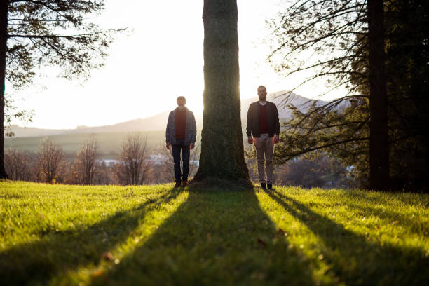 istock Senior father and his son standing by tree at sunset, looking at camera. 1168602615