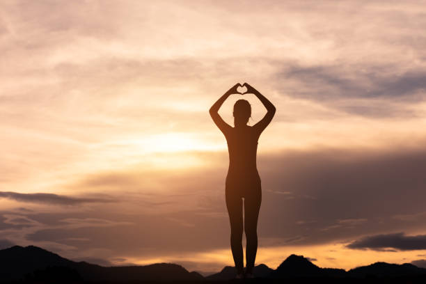silhouette girl standing on top of mountain and making heart shape stock photo