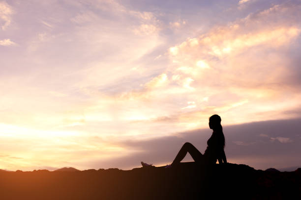 silhouette woman sitting and relaxing on top of mountain stock photo