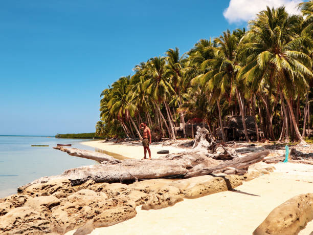 Man walking on the white beach and turquoise water with clear blue sky and lots of palm trees on Sicsican Island in Balabac, Palawan, Philippines