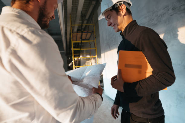 istock Industrial architect discussing build drawing with worker wearing safety hard hat. Two building engineers lookin at blueprint on construction site 1168610468