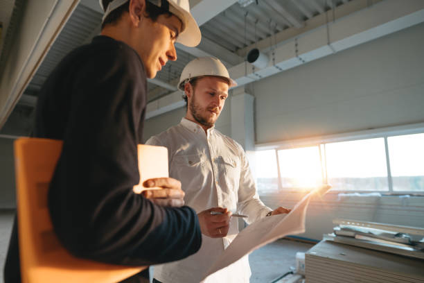 Building industry. Young engineer discussing with building worker on construction site. Industrial engineers have meeting while uses blueprint