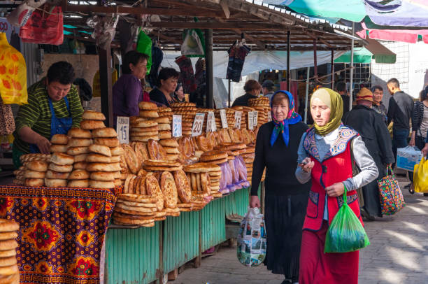 Non bread display at the street market Bishkek, Kyrgyzstan - September 25, 2018: Rows of food stalls at Osh Bazaar, selling traditional central asian round, flat bread Non or Naan and local people walking along with goods in hand bishkek photos stock pictures, royalty-free photos & images