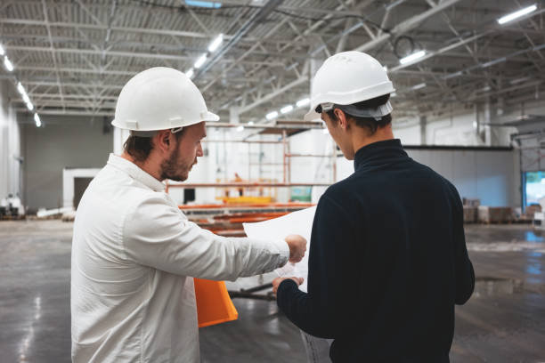 istock Building industry. Young engineer discussing with building worker on construction site. Industrial engineers have meeting while uses blueprint 1168611309