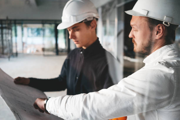 istock Industrial architect discussing build drawing with worker wearing safety hard hat. Two building engineers lookin at blueprint on construction site 1168611319