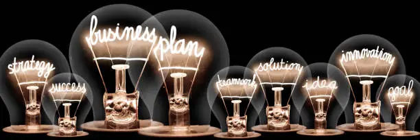 Large group of light bulbs with shining fibers in a shape of Business Plan, Strategy, Innovation and Success concept related words isolated on black background