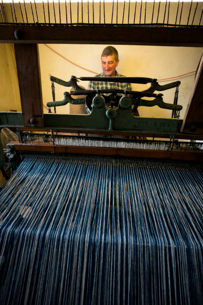 A male crofter busy at work on an older, smaller Hattersley foot-powered loom at home weaves wool sheared, dyed and spun on the island according to Parliment bylaws to create distinctive tweed cloth fabric on the Isle of Lewis, Outer Hebrides, Scotland, UK
