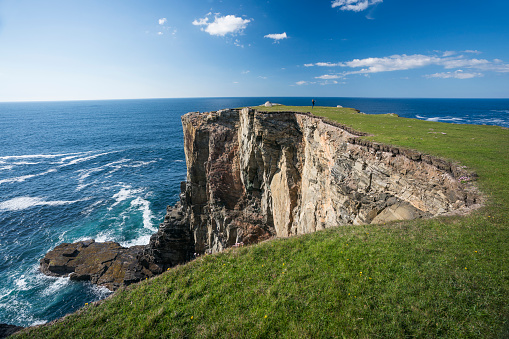 Tourist walks out on the rocky peninsula jutting out to sea on the cliffside walk heading north from Dalbeg Beach, Dail Beag, on the Atlantic Ocean on the northwest side of the Isle of Lewis in the Outer Hebrides, Scotland, UK, Europe