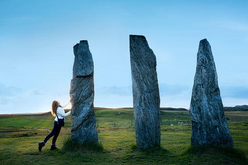 Female tourist looks up at a trio of tall rocks at the famous Calanais Standing Stones, Outer Hebrides, Isle of Lewis, Scotland, UK.