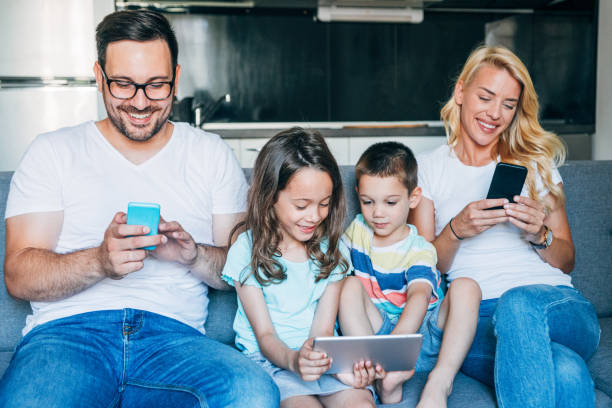 Relaxing at home with wireless technology Portrait of a smiling young family with two kids holding smart phones and digital tablet at home. family dependency mother family with two children stock pictures, royalty-free photos & images