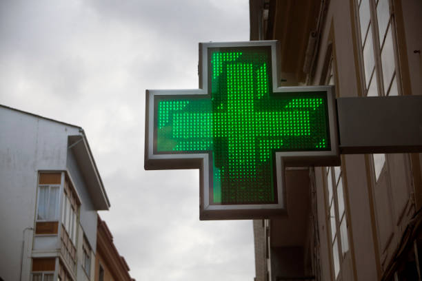 simbolo della farmacia per strada, edifici alti, croce verde. - green cross foto e immagini stock