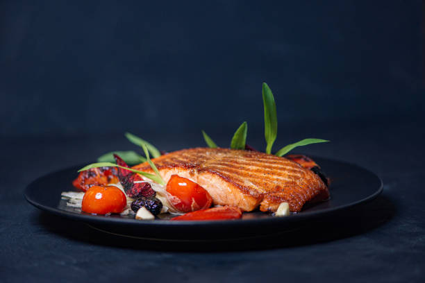 おいしい食べ物。黒皿にハーブと野菜を入れたサーモンステーキ、クローズアップ。 - prepared fish fish grilled close up ストックフォトと画像
