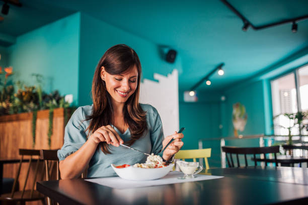 mujer positiva comiendo ensalada en un acogedor café. - comer fotografías e imágenes de stock