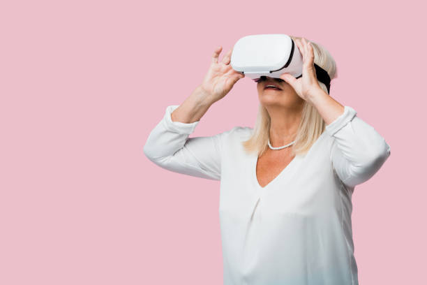 istock retired woman wearing virtual reality headset isolated on pink 1168616152
