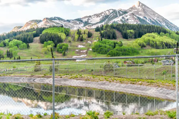 Mount Crested Butte Colorado peak in summer with reflection view in lake reservoir from Snodgrass trail behind fence