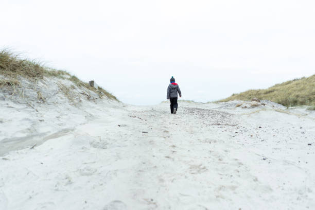 das kind geht in die ferne auf den sanddünen - winter cold footpath footprint stock-fotos und bilder