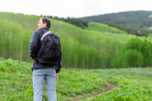 Man standing back with backpack on Snodgrass trail with bokeh background view of aspen forest in Mount Crested Butte, Colorado in summer