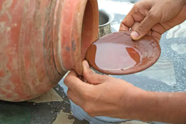 Human hand filling earthen pot with drinking water