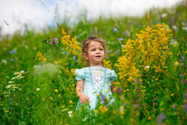 Little girl wearing blue dress standing in garden of grass and flowers