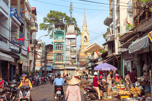 Ho Chi Minh City, Vietnam - May 1, 2019: a picturesque street of Cholon occupied by market activity, with a view of townhouses and Cha Tam Church (St. Francis Xavier Parish Church).