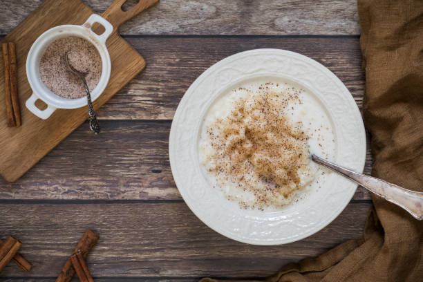 Rice pudding with ground cinnamon flat lay from above perspective Traditional Swedish rice pudding with ground cinnamon flat lay from above perspective. There is a small bowl with cinnamon and sugar on a wooden chopping board next to the food. porridge stock pictures, royalty-free photos & images
