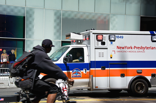 New York City, USA - June 08, 2019: A bicyclist watches an ambulance passing by along 57th St
while it responds to an emergency call, Upper Midtown Manhattan.