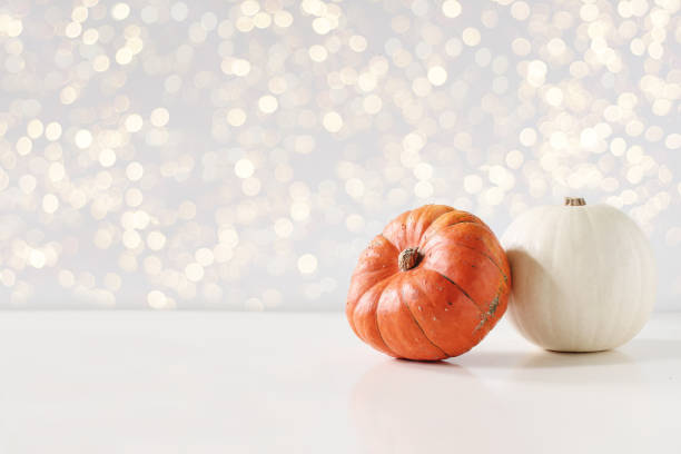 istock Modern autumn styled composition. White and orange pumkins on white table background. Halloween, Thanksgiving party concept. Festive fall design with golden sparkling bokeh lights. Empty space. 1168639395