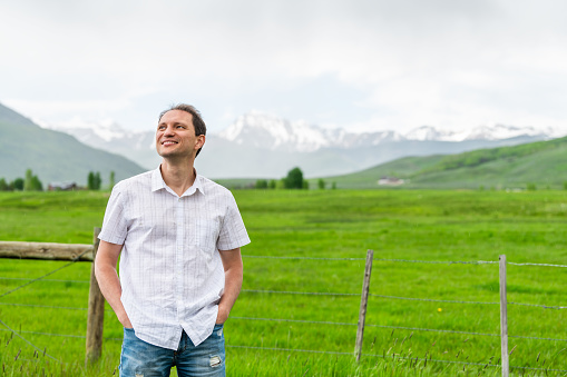 Crested Butte, Colorado countryside with happy young man standing by fence and in summer on cloudy day with green grass and mountain view