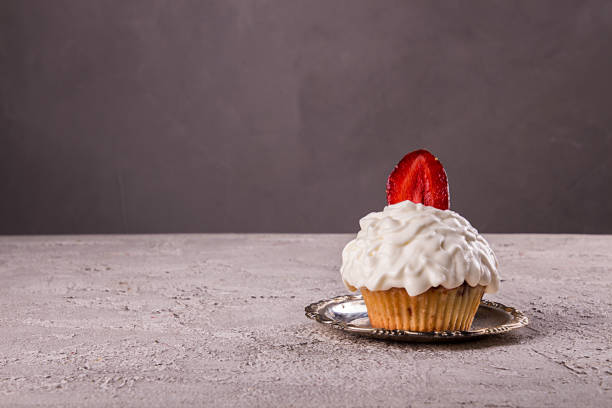 Cupkake with whipped cream decorated with strawberry on top on gray background. Copy space
