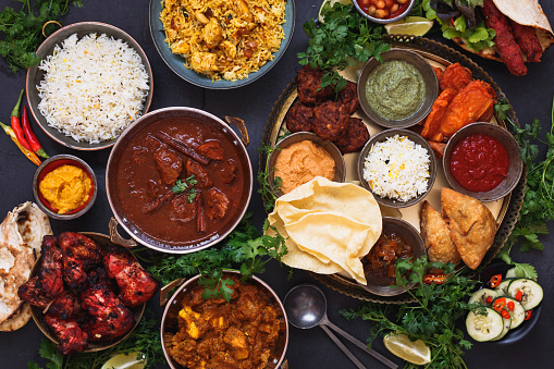 Various Indian dishes featuring  rogan josh, chicken tikka masala, biryani, tandoori chicken, kebabs and mixed indian platter with samosa, pakoras, onion bajis, poppadoms , naan and dips, top view