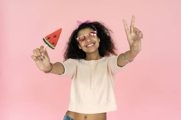 счастливый улыбающийся игривый молодой афро-американский подросток девушка черная женщина носить стильные очки очки держать арбуз конфет - gen z стоковые фото и изображения