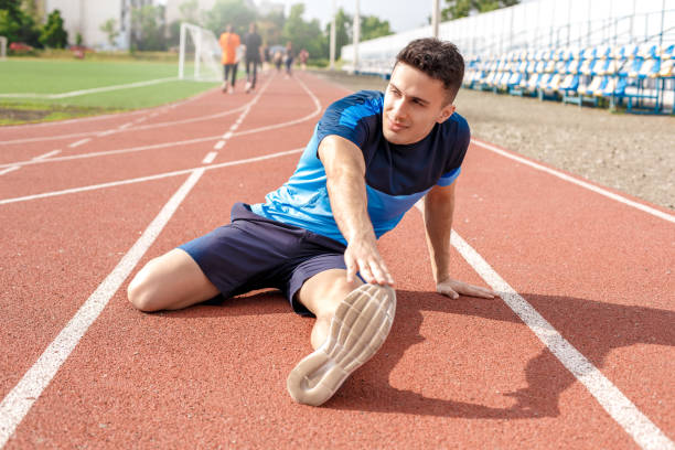 istock Marathon preparation. Young man on track outside stretching legs smiling motivated 1168662828