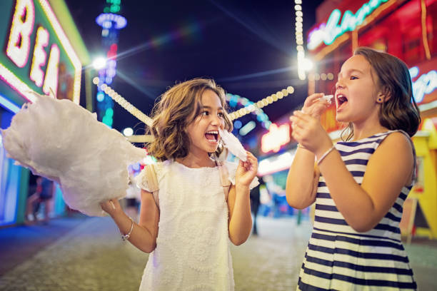 Two little girls are eating cotton candy at the fun fair and making fun Two little girls are eating cotton candy at the fun fair and making fun child cotton candy stock pictures, royalty-free photos & images
