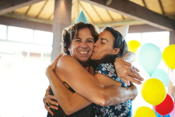 mother and daughter embracing and celebrating a birthday party using party hat - life events laughing women latin american and hispanic ethnicity imagens e fotografias de stock