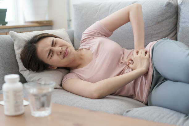 asian woman with menstruation and pain period cramps. young women having painful sleeping on sofa at her home stock photo