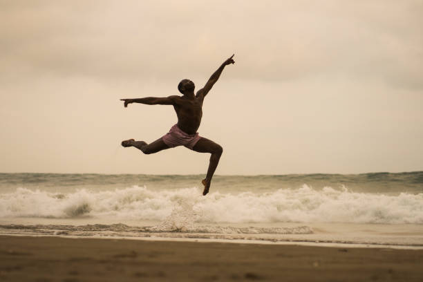 istock dramatic contemporary dance choreographer doing ballet beach workout . young attractive and athletic black African American man dancing on sunrise jumping elegant and with amazing plasticity 1168701394