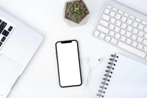 Modern white office work table with smartphone mock up laptop ,earphone and catus, top view