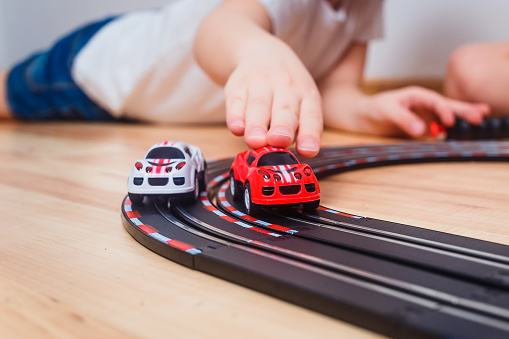the child rolls small cars on a toy car track indoors